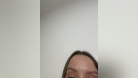 A video featuring a close-up of a person's face, with light skin, brown hair, and a slight smile. The background is a plain white wall, creating a minimalistic and clean aesthetic.
