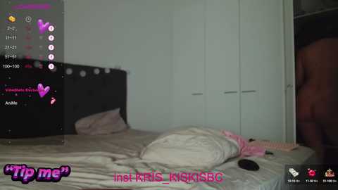Video of a dimly lit bedroom with a white bed, a black headboard, and a partially visible man in the corner, with an open closet in the background.