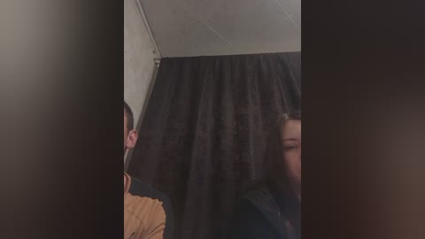 Video of a dark curtain partially covering a bathroom ceiling, with a person's face visible on the right, wearing a dark top, and another person's head, with brown hair, visible on the left.