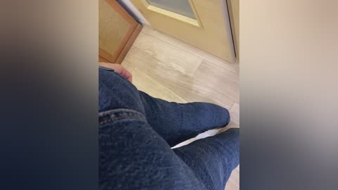 Media: Video of a person wearing blue jeans and a white shirt, lying on a beige carpet in a hallway with light wooden floors and a glass door.