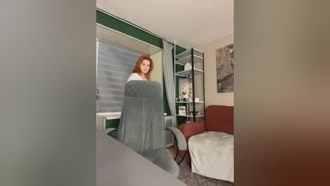 Media: A video of a woman with red hair, wrapped in a grey towel, standing in a modern living room with green walls, white blinds, and a grey armchair.