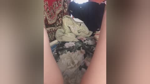 A video shows a messy bed with crumpled sheets, a red and gold tapestry, and a black garment in the background, likely in a dimly lit bedroom.