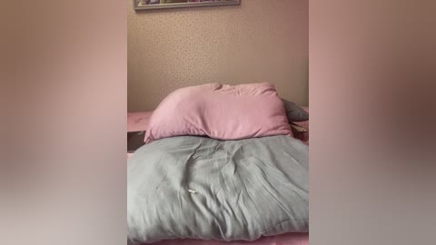 Video of a cozy, messy bedroom with a pink pillow and a light blue duvet, set against a beige textured wall, featuring a framed picture at the top.