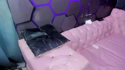 Video of a modern, pink upholstered sofa with a tufted design, featuring a black marble pillow and a white remote control on the cushion. The background wall has a hexagonal pattern with purple LED lighting.