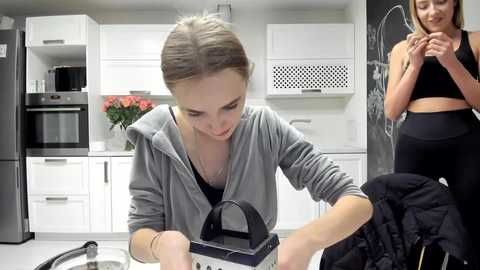 Media: Video of a woman in a gray hoodie, focused on a black iron, in a modern white kitchen with black appliances and a chalkboard wall.