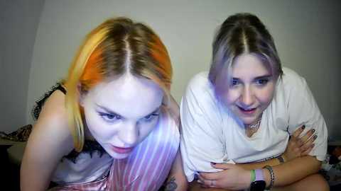 Media: Video of two young women with dyed hair (orange and black) wearing casual clothing; one with a tattooed arm, the other smiling.