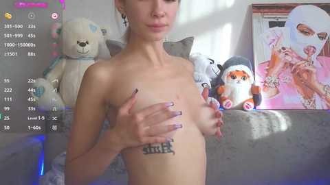Media: Video of a slender, topless young woman with small breasts, holding her chest, standing in a bedroom with plush toys and anime posters.