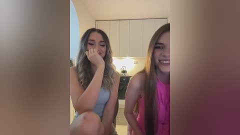 Media: Video of two young women in a kitchen, one covering her face with her hand, the other smiling.