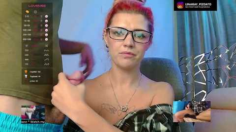 A video of a red-haired woman with glasses, wearing a black off-shoulder top, and a tattoo on her chest, seated in a dimly lit room, holding a microphone.