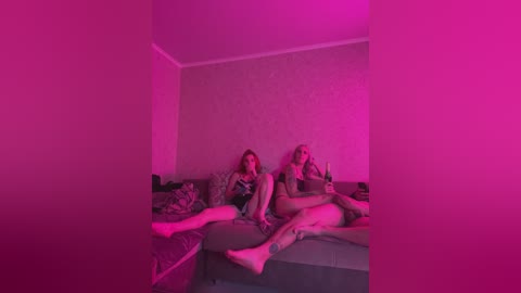 Media: A video featuring two women in a dimly-lit, pink-hued room, lying on a bed, one holding a phone, the other a drink, surrounded by disheveled bedding.