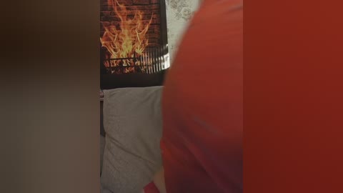 Media: Video of a cozy bedroom with a burning fireplace in the background, showcasing a plush, orange blanket and a grey pillow on the bed. The room has a warm, inviting ambiance.