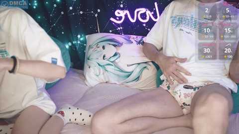 Media: Video of two young adults in a bedroom, one in white polka-dot shorts, the other in a floral onesie, lounging on a bed with a \"Sailor Moon\" pillow, a starry backdrop, and digital overlays.