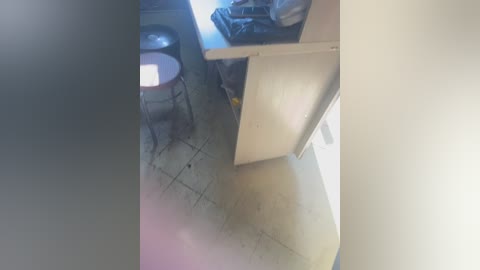 Media: A video of a dimly lit, small kitchen with a wooden countertop, a metal stool, and a tiled floor. The room appears cluttered with appliances and miscellaneous items.