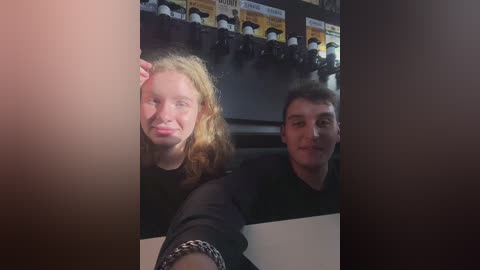 Media: Video of two people, a blonde woman and a man with short hair, smiling and making faces. Background shows a wall with \"FILM\" signs.