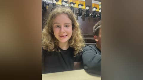 Media: Video of a young girl with curly brown hair, smiling, sitting at a table with a man in a black shirt in the background.