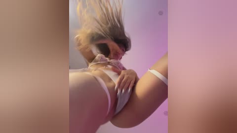 Media: A video of a woman in a white lace bra and panties, hair flying, captured from a low angle, with a pink and purple gradient background.