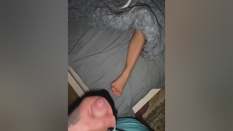 Media: Video of a sleeping woman in a grey quilted blanket with a barefoot man lying next to her on a beige-patterned bedspread.