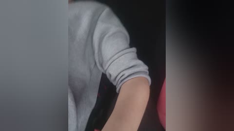 Media: A close-up video of a person with light skin wearing a gray long-sleeved shirt, bending forward, with a dark background. The image is blurry and lacks detailed context.