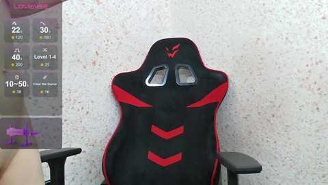 Video of a black gaming chair with red accents, featuring a headrest with two small side windows, set against a speckled white wall. In the background, a virtual gaming overlay displays stats like \"Level 4,\" \"Health 30,\" and \"Ammo 10.\