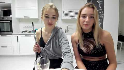 Media: Video of two young women in a modern kitchen; one with blonde hair in a grey hoodie, the other with long blonde hair in a black fishnet top.