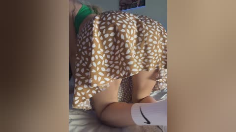 Video of a woman in a brown skirt with white polka dots, kneeling on a bed, with her legs spread and visible underwear.
