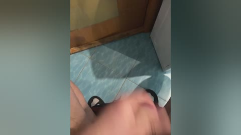 A video shows a person's head in motion, partially obscured by a blue-tiled floor, a wooden door, and a white wall, with a yellowish patch in the background.