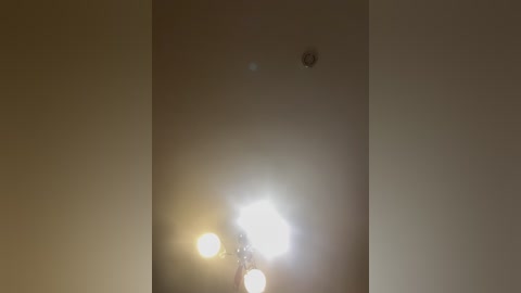 A video of a dimly lit room with a single, bright light source creating a halo effect, casting a soft glow on the plain, beige walls.
