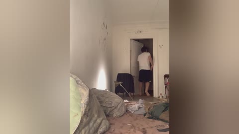 A video captures a messy, beige-painted room with a partially open door revealing a person in white and blue standing in a doorway.