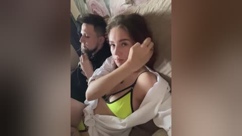 Media: Video of a young woman with long brown hair and a man with short black hair, both lying on a bed, wearing neon green lingerie.