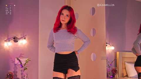 A video of a young woman with bright red hair, wearing a ribbed gray crop top and black mini skirt, standing confidently in a dimly lit bedroom with purple lighting.
