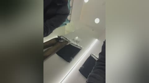 Media: Video of a hand holding a knife over a black wallet on a white counter. The scene appears dimly lit with a blurry background.