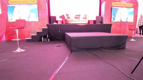 Media: Video of a stage with a black curtain backdrop, red chairs, and two screens displaying \"Vongacam.com\" logos.