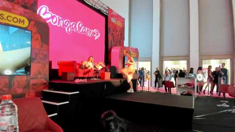 Media: Video of a lively indoor event with a large pink \"Bongacams\" banner, a stage with dancers, audience members, and promotional banners.