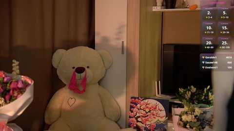 Media: A video of a plush teddy bear with a pink ribbon in a cozy room with a TV, flowers, and a calendar screen.