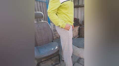 Media: Video of a person wearing a yellow and white striped shirt, white pants, and seated on a gray cushioned chair in an outdoor, rustic setting with stone walls and a wooden bench.