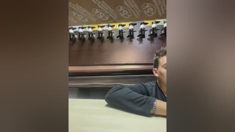 Media: Video of a man in a dark shirt, face partially obscured, lying on his stomach on a beige carpet, under a row of bowling pins and a wooden ball return.