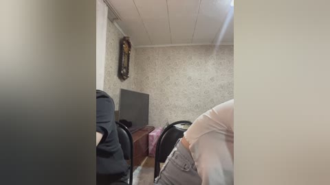 A video of an office interior with beige floral-patterned wallpaper, a black chair, a desk, and a flat-screen TV, viewed through a partially obstructed doorway.