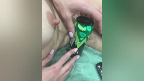 A close-up video shows a person with fair skin, wearing a green bikini top, manipulating a green can with a black lid. The background is blurred with a green gradient.