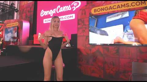 Media: Video of a blonde, fit woman in a black one-piece swimsuit posing confidently in front of a red brick wall with \"Bongacams.com\" and \"BongaCams\" logos.