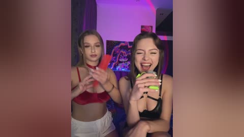 Media: Video of two women dancing in a dimly lit room. One wears a red bra and white shorts, the other a black bra. They have fair skin and are smiling, with neon green nails.