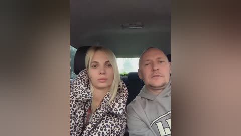 Media: Video of a blonde woman and a bald man in a car, both looking tired, wearing leopard print and gray hoodies, respectively.