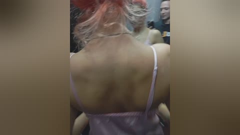 Video of a woman with pale skin and pink hair, wearing a white camisole, standing in a dimly lit room, with a security guard in the background.