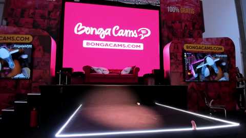 Media: Video of a vibrant stage setup featuring a large pink screen with \"BongaCams.com\" logo. Two large screens on either side display live streaming content. Red and black decor, including a couch, create a dynamic, modern backdrop.