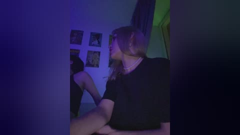 A dimly lit video of a young woman with long blonde hair, wearing a black top and pearl necklace, examining a framed photo in a dimly lit room with blue and purple lighting.