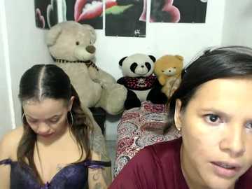 Video of a woman with long dark hair, wearing a maroon shirt, sitting on a bed adorned with a plush panda bear, a teddy bear, and a floral pillow.