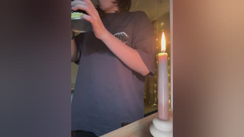 Media: A video of a person with a light skin tone, wearing a dark blue t-shirt, holding a smartphone, with a lit candle beside them, creating a cozy, warm atmosphere in a dimly lit room.