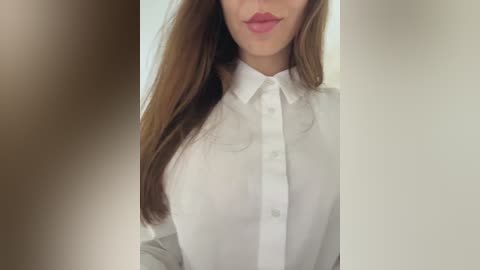 Media: Video of a woman with fair skin, long brown hair, and full lips, wearing a white button-up shirt, partially blurred in the foreground.