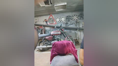 Media: Video of a cluttered, dimly lit workshop with multiple motorcycles, a red triangle road sign, and a man in a purple shirt visible from the back, working on a bike.