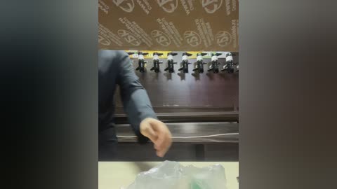 Media: Video of a person in a dark suit and tie, gesturing with their left hand, standing in front of a row of industrial pumps. Background features a brown wall with white text.
