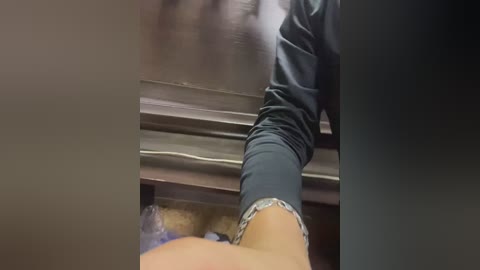 Media: Video of a person with light skin, wearing dark pants, sitting on a wooden floor with visible electrical wires and a plastic bag in the background.